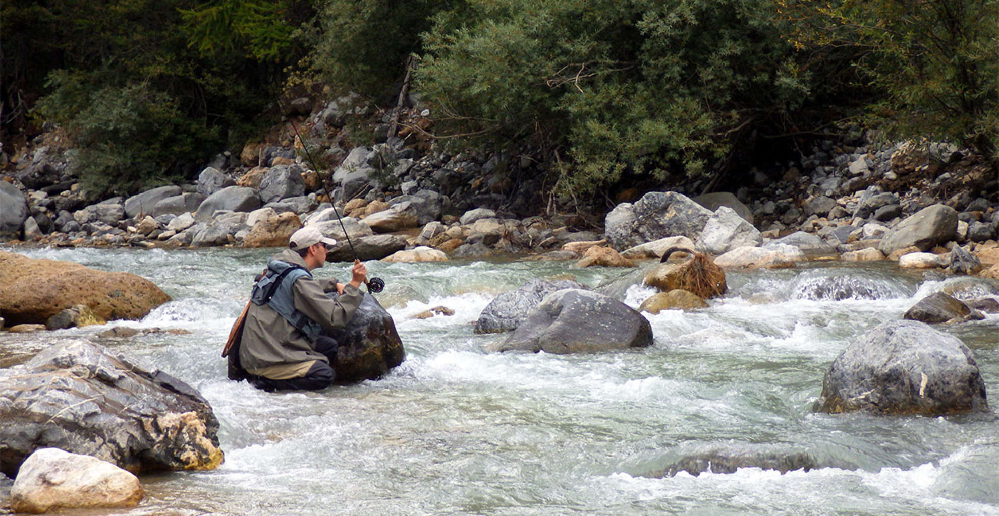 Pêcheur à la mouche dans une rivière rocheuse au relief marqué